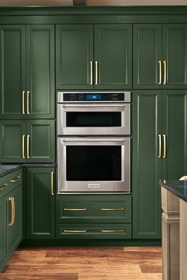 Close-up of a green Thomasville Oven Microwave Combo Cabinet, featuring stainless steel appliances and gold handles, part of a modern kitchen with ample storage.